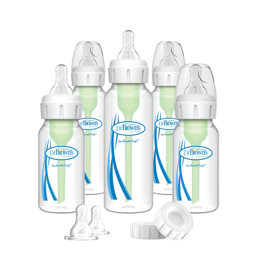 A set of five Dr. Brown's Natural Flow® Anti-Colic Options+™ narrow baby bottles, including green internal vent systems, prominently displayed alongside extra bottle nipples and travel caps in the foreground. These clear bottles feature anti-colic benefits, complete with white caps and highlighting blue logos and design elements.