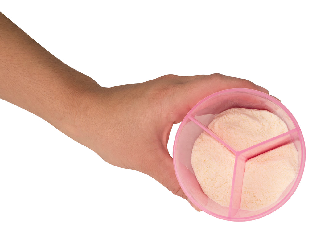 A hand holding Dr. Brown's Dr. Brown’s® Baby Formula Dispenser, a pink container with three compartments filled with light pink baby formula powder, viewed from above.