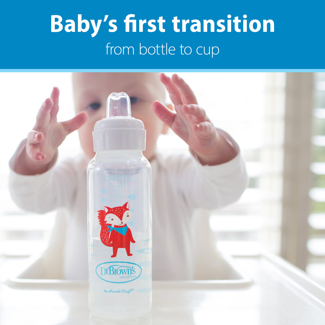 A baby reaches for a Dr. Brown's® Milestones™ Narrow Sippy Bottle while sitting in a high chair adorned with a fox design. Above, the text states, "Baby’s first transition from bottle to cup." The soft silicone spout ensures comfort as natural light filters through the blinds in the background.