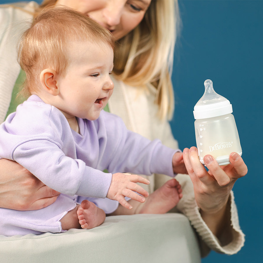 Woman holding a baby and a Dr. Brown's Silicone Baby bottle with a blue background