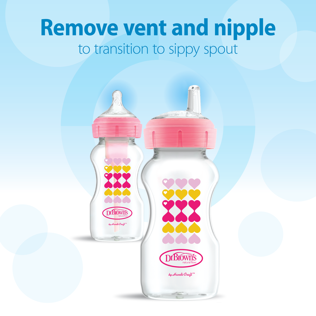 The image displays two Dr. Brown's Natural Flow® Anti-Colic Options+™ Wide-Neck Sippy Bottles, each with a pink top. One bottle is equipped with a regular nipple, perfect for minimizing colic during feeding, while the other features a silicone sippy spout. Both bottles are decorated with colorful hearts on the front. Above them, text instructs to "Remove vent and nipple to transition to sippy spout.