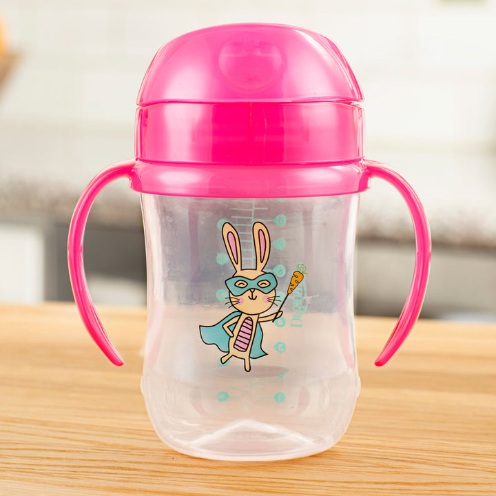 Introducing the Dr. Brown’s® Soft-Spout Toddler Cup, a 9 oz/270 ml (9m+) product that features a transparent design with a playful cartoon rabbit superhero holding a carrot. Equipped with a pink lid and handles, this cup's silicone spout is perfect for spill-free transitions from bottle to cup, all accentuated by the blurred kitchen background in its imagery. This product is brought to you by Dr. Brown's.