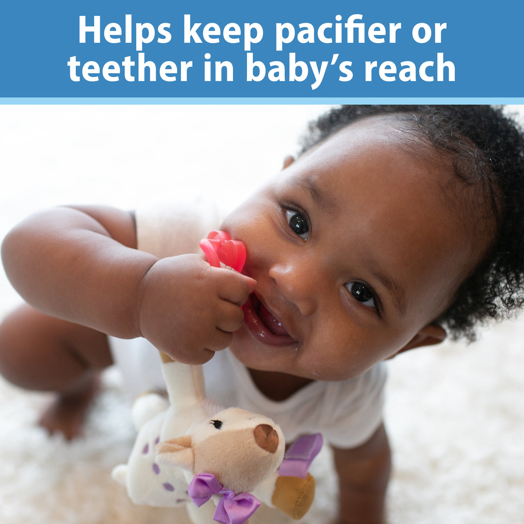 A baby, happily sitting on the floor in a white onesie, holds a teether while Dr. Brown's Dr. Brown’s® Lovey Pacifier and Teether Holder, Deer is nearby. Text above reads, "Helps keep pacifier or teether in baby's reach.