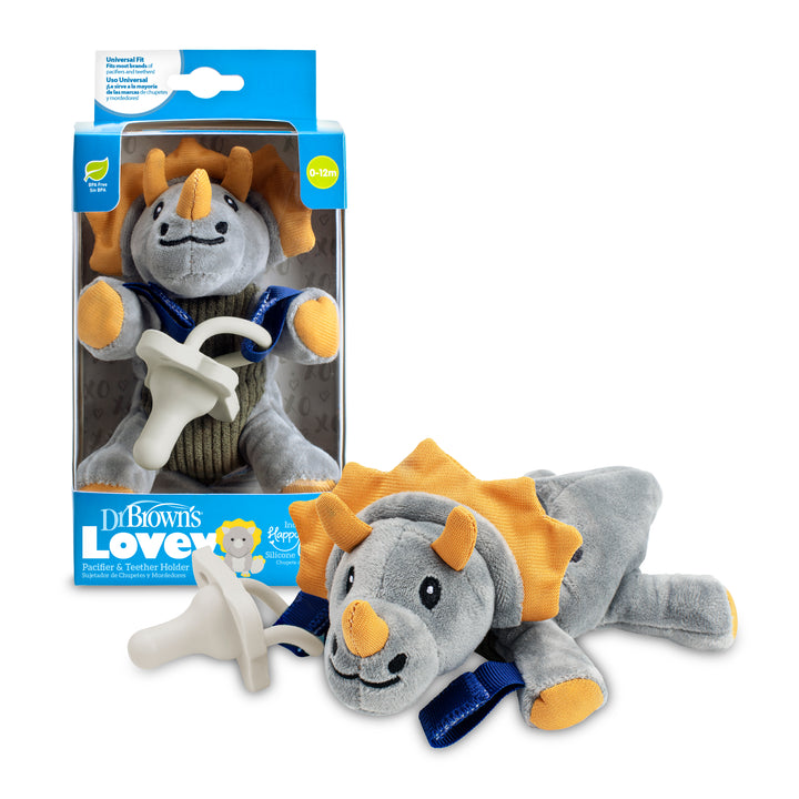 A plush gray triceratops toy with orange accents is affixed to a white pacifier, resting next to its packaging. The box showcases the toy and reads "Dr. Brown’s® Lovey Pacifier and Teether Holder, Triceratops," ideal for newborns to 12 months.