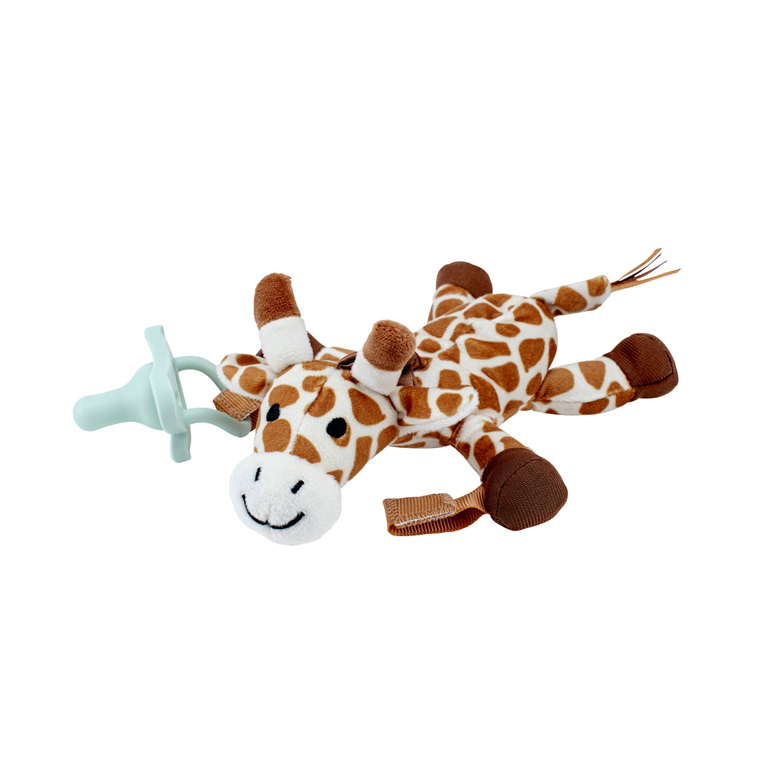 A Dr. Brown's® Lovey Pacifier and Teether Holder, Giraffe, featuring brown and white spots, is shown lying flat with a Dr. Brown’s HappyPaci attached to its body. This giraffe has a smiling face, small brown horns, and its legs and tail extended outward.