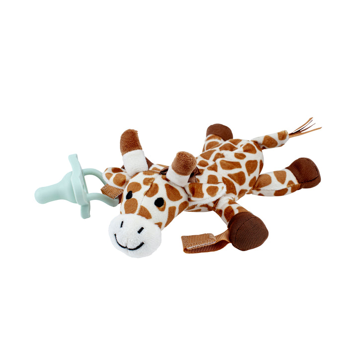 A Dr. Brown's® Lovey Pacifier and Teether Holder, Giraffe, featuring brown and white spots, is shown lying flat with a Dr. Brown’s HappyPaci attached to its body. This giraffe has a smiling face, small brown horns, and its legs and tail extended outward.