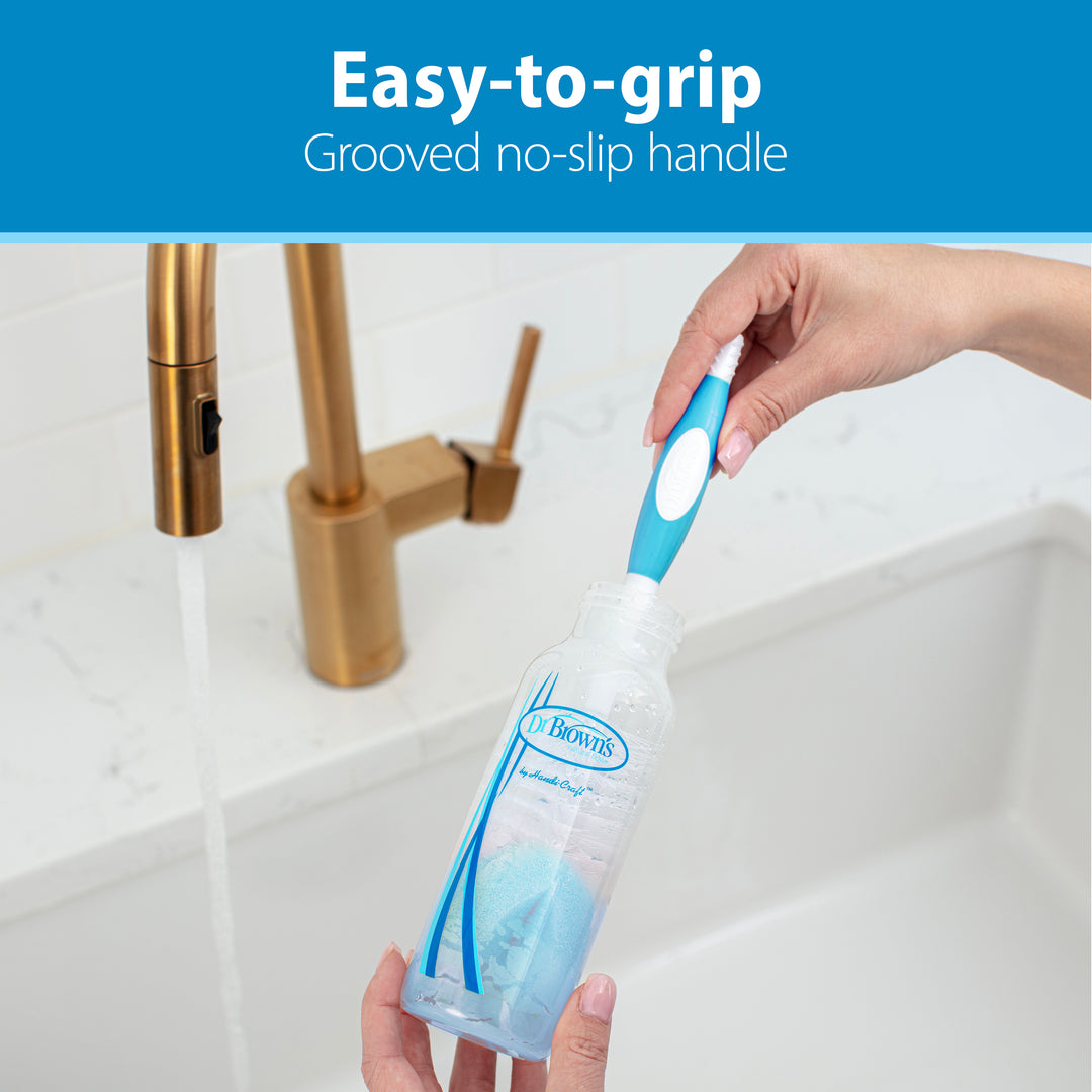 Hands using the Dr. Brown’s Natural Flow® Baby Bottle Brush with an easy-to-grip, grooved handle to clean a baby bottle under running water. Ideal for baby bottles, this brush features an integrated nipple cleaner. The text above states, "Easy-to-grip Grooved no-slip handle.