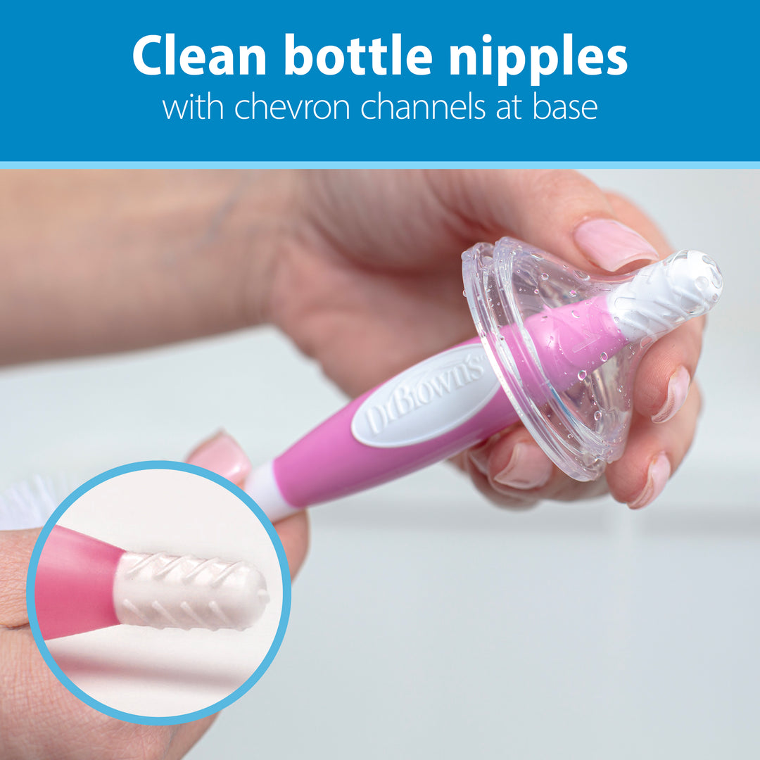 A close-up shows hands holding a Dr. Brown’s™ Soft Touch Bottle Brush with a pink and white handle. The brush tip is inserted into a transparent bottle nipple, which features chevron channels at its base designed for scratch-free scrubbing. At the top, text reads, "Clean bottle nipples with chevron channels at base.