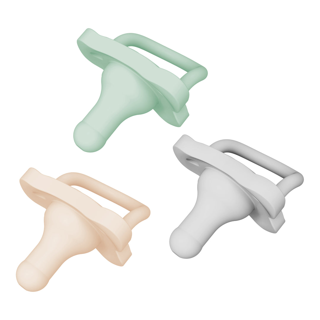 Three pastel-colored pacifiers—green, peach, and white—are arranged in a triangular pattern on a white background. Crafted from silicone, each Dr. Brown’s® HappyPaci™ 100% Silicone One-Piece Pacifier features a straight handle and a rounded bottle nipple shape for natural comfort.