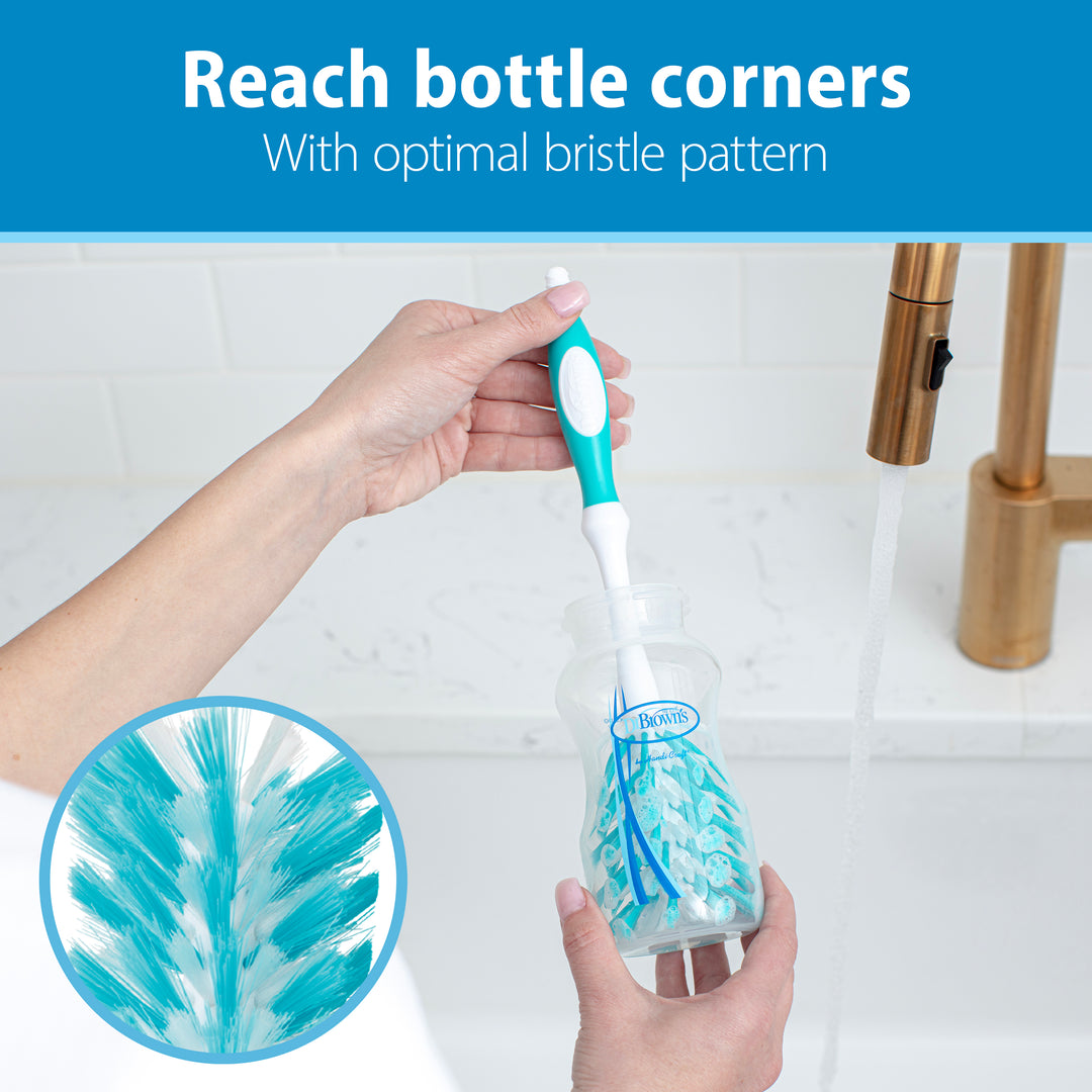 A person uses the Dr. Brown’s Natural Flow® Deluxe Bottle Brush, colored in blue and white, to clean a transparent bottle under a faucet. A close-up inset highlights its BPA-free bristles. Text above reads, "Reach bottle corners with optimal bristle pattern.