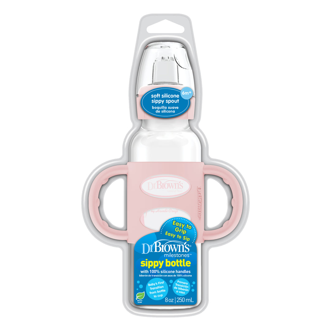 The Dr. Brown’s® Milestones™ Narrow Sippy Spout Bottle with Silicone Handles comes with a pink silicone holder and large silicone handles. The clear bottle, featuring blue and white labeling, has a capacity of 8 oz (250 mL) and is equipped with a soft sippy spout ideal for babies aged 6 months and older.