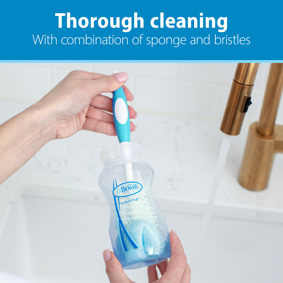 An individual utilizes the Dr. Brown’s Natural Flow® Baby Bottle Brush by Dr. Brown's, featuring a blue and white design with bristles and a sponge tip, for effectively cleaning baby bottles under running water in a sink. The packaging reads, "Thorough cleaning with combination of sponge, bristles, and nipple cleaner.