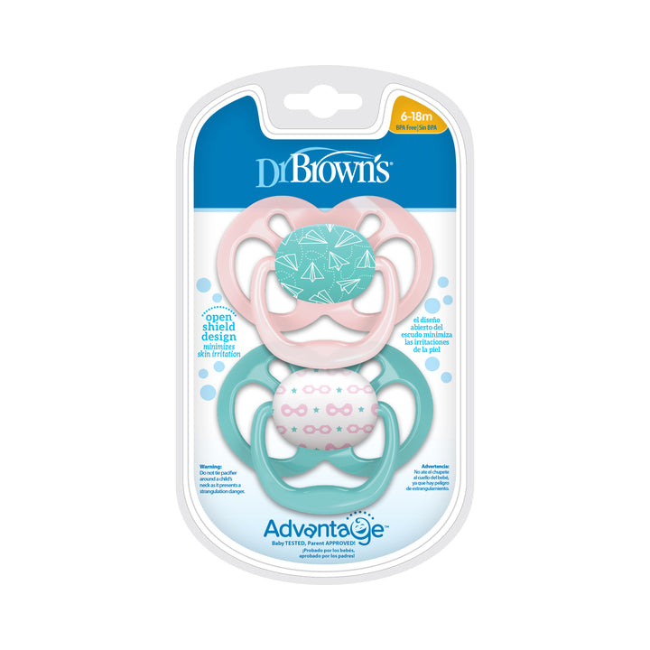 Product packaging for Dr. Brown’s™ Advantage™ Pacifiers, 2 count, includes two open shield design soothers. The top pink pacifier features a paper airplane pattern, while the bottom teal one showcases a heart and triangle design. These pacifiers have a symmetrical, reversible bulb and are suitable for ages 6-18 months.