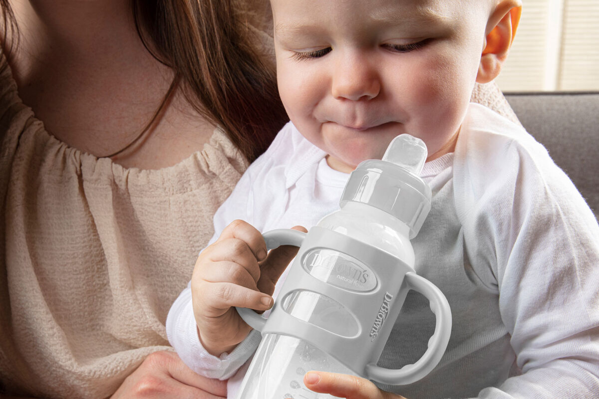 Baby holding a Dr. Brown's Sippy Bottle with silicone handles whiel sitting on his mom's lap
